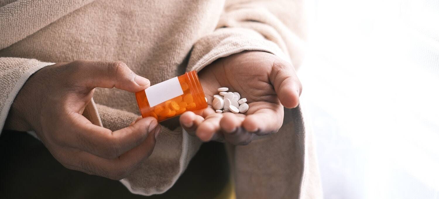 Person pouring out pills from prescription pill bottle into hand